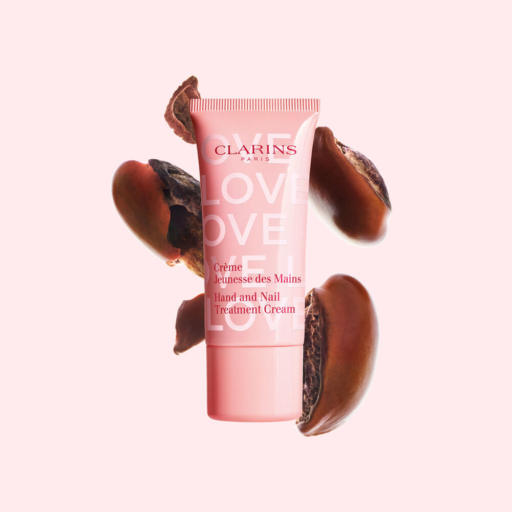 Plan produit de la cr&egrave;me pour les mains de la collection Love en &eacute;dition limit&eacute;e sur un fond rose clair avec des graines de karit&eacute; mettant en valeur l&rsquo;ingr&eacute;dient cl&eacute; du produit