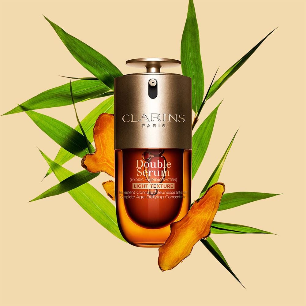 Un flacon de 30 ml de Double Serum Light Texture de Clarins avec du curcuma et des feuilles de grand roseau de Provence sur un fond orange.