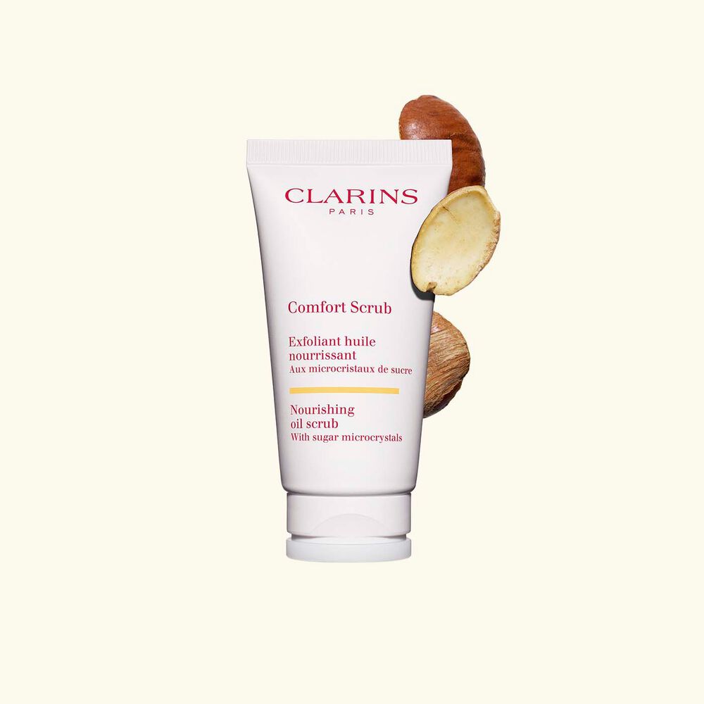Plan produit du tube de l’exfoliant visage et lèvres Comfort Scrub à côté de quelques graines de mangue sauvage sur fond beige