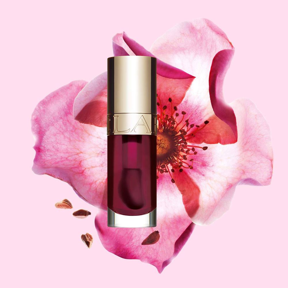 Plan produit de l’Huile Confort Lèvres Clarins en teinte Fig avec une rose musquée sur fond couleur rose clair.