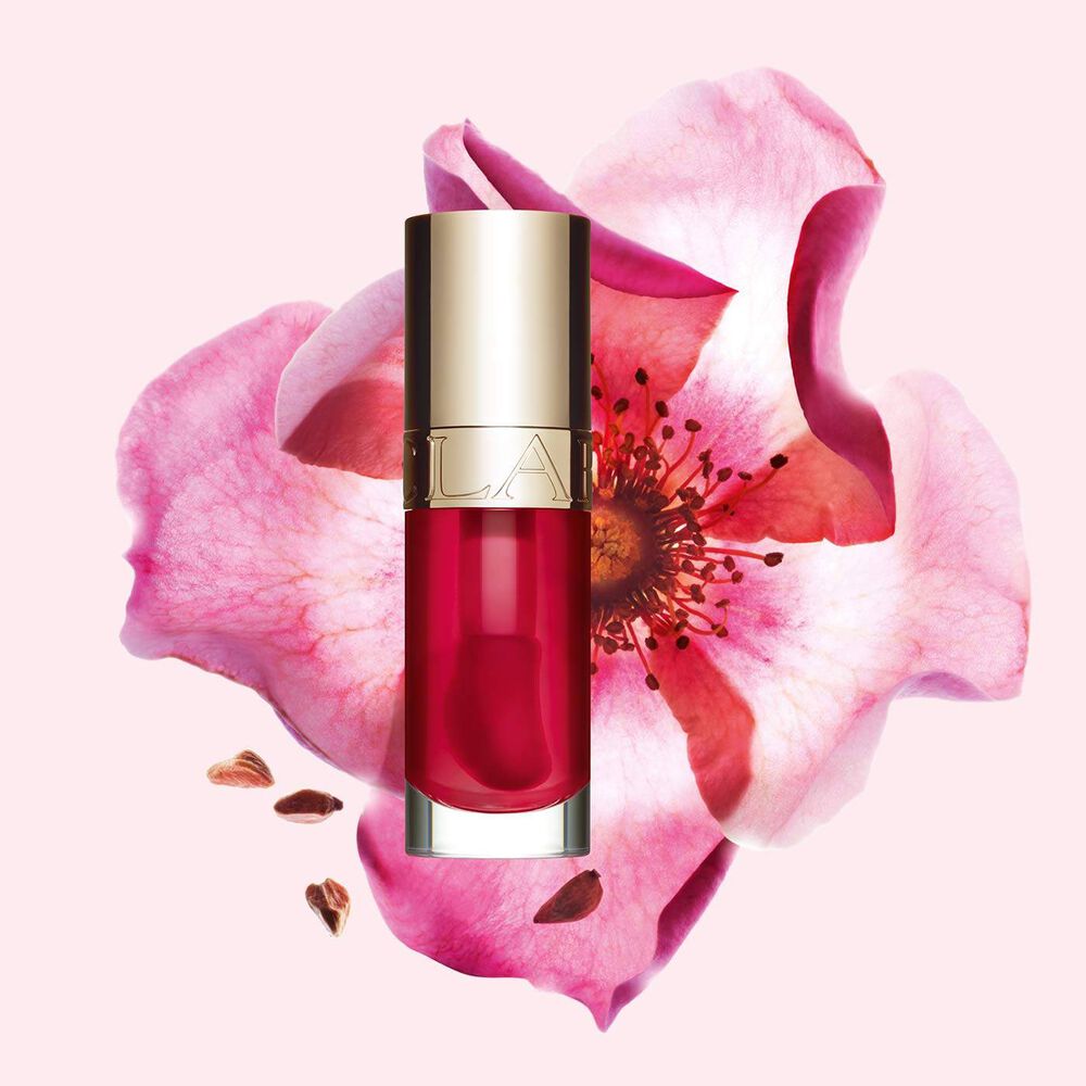 Plan produit de l’Huile Confort Lèvres Clarins en teinte Fuchsia avec une rose musquée sur fond couleur rose clair.