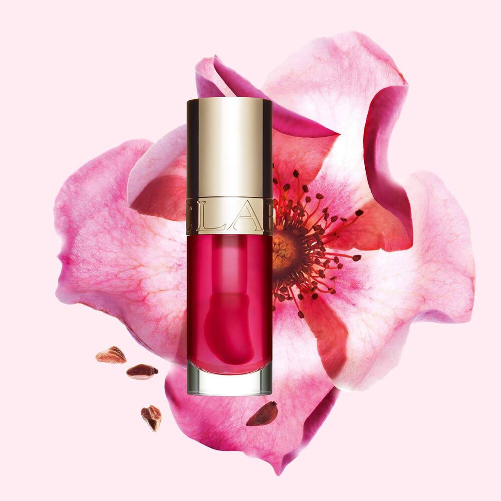 Plan produit de l’Huile Confort Lèvres Clarins en teinte Pitaya avec une rose musquée sur fond rose clair.
