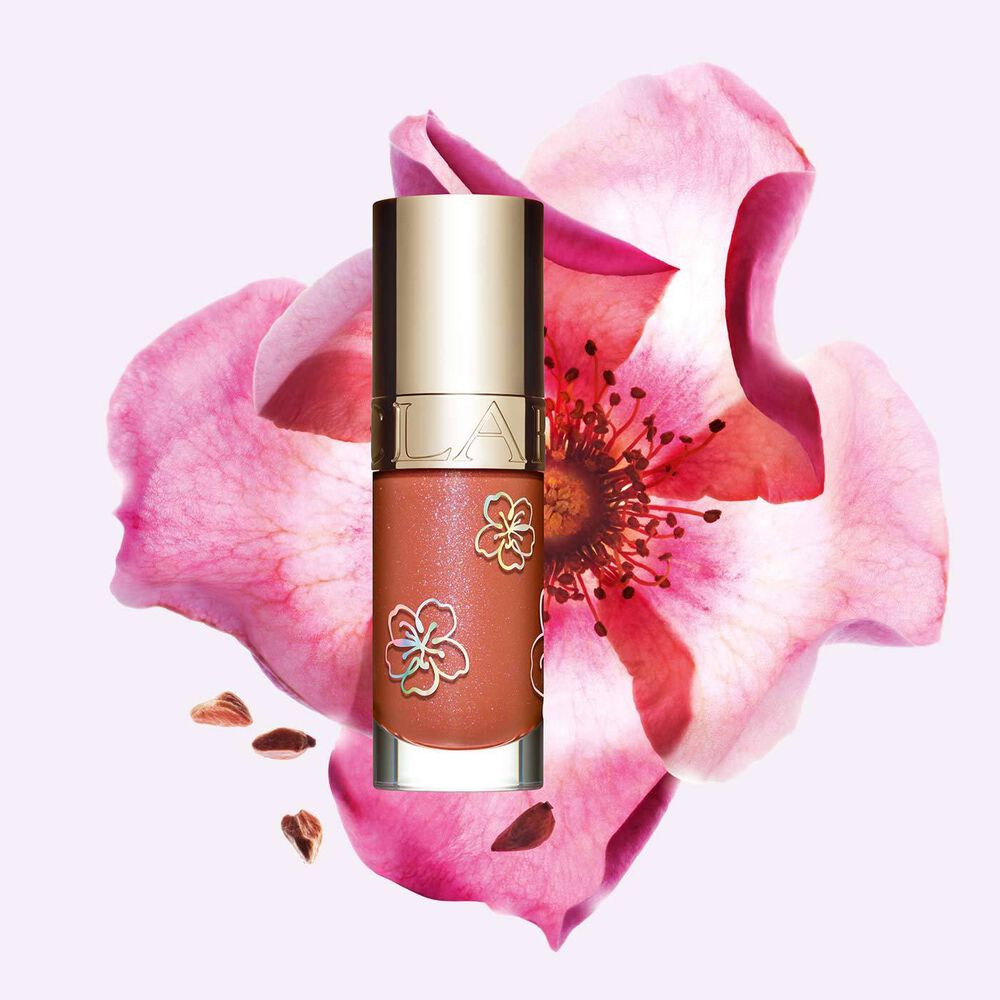 Plan produit du Lip Comfort Oil Clarins couleur Rosy Sakura, un produit à lèvres en édition limitée dans une teinte rose, à côté d'une fleur.