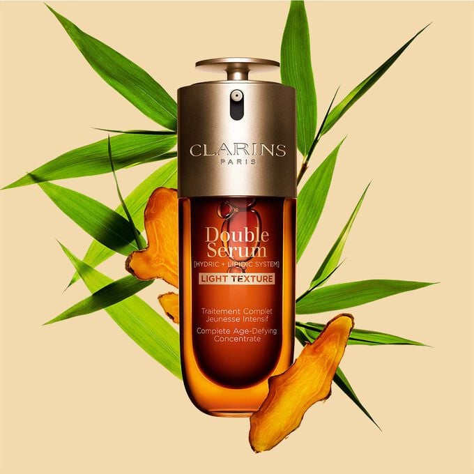 Un flacon de 50&nbsp;ml de Double Serum Light Texture de Clarins avec du curcuma et des feuilles de grand roseau de Provence sur un fond orange.