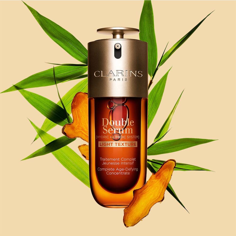 Un flacon de 70&nbsp;ml de Double Serum Light Texture de Clarins avec du curcuma et des feuilles de grand roseau de Provence sur un fond orange.