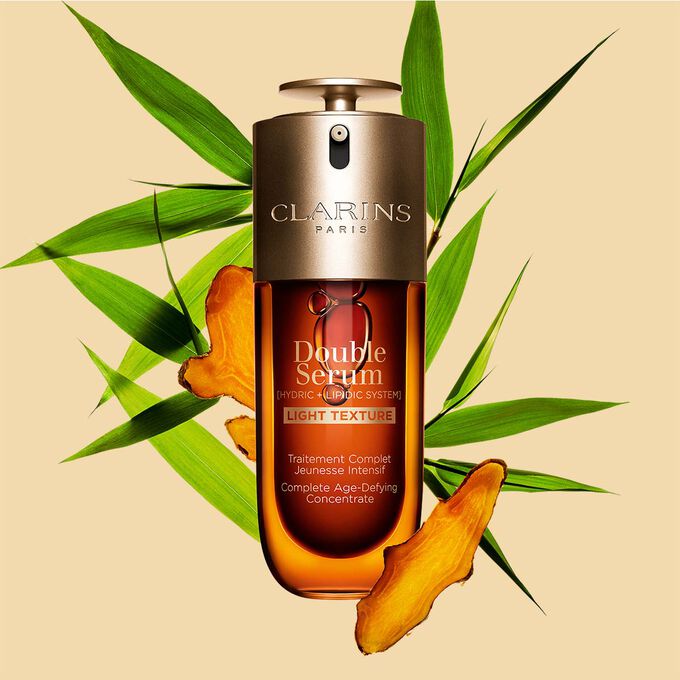 Un flacon de 70&nbsp;ml de Double Serum Light Texture de Clarins avec du curcuma et des feuilles de grand roseau de Provence sur un fond orange.