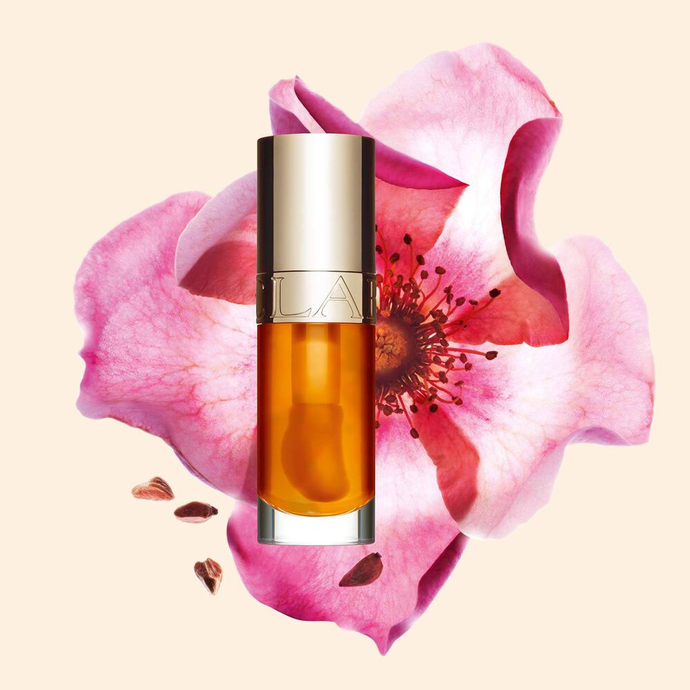 Plan produit de l’Huile Confort Lèvres Clarins en teinte Honey avec une rose musquée sur fond couleur pêche clair.