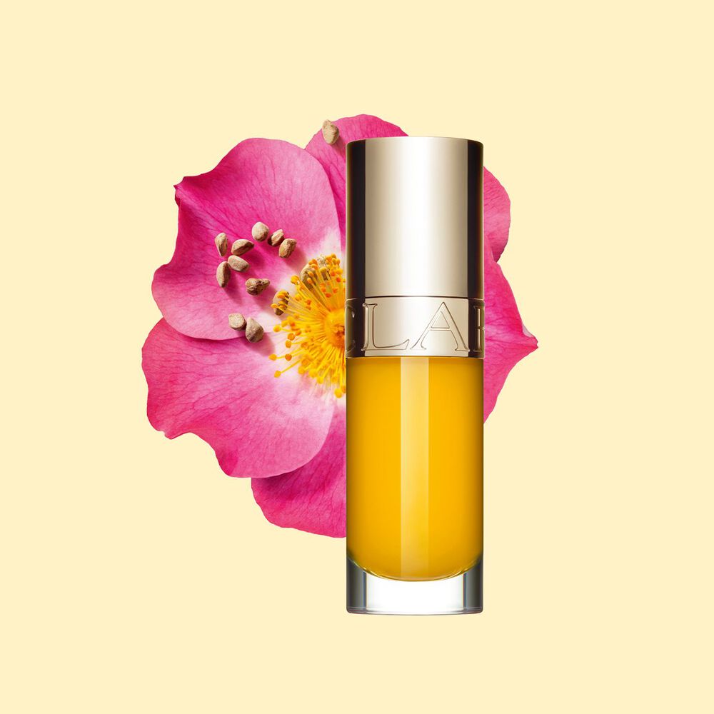 Plan produit de l’huile lèvre jaune Clarins devant une fleur de rosier rouillé sur fond blanc