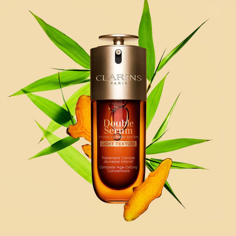 Un flacon de 70 ml de Double Serum Light Texture de Clarins avec du curcuma et des feuilles de grand roseau de Provence sur un fond orange.