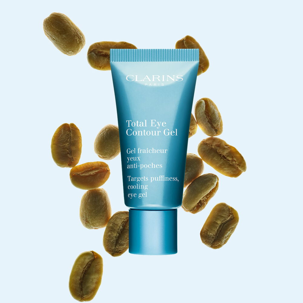 Tube du Total eye contour gel de Clarins pr&eacute;sent&eacute; avec des grains de caf&eacute; verts sur un fond bleu clair.