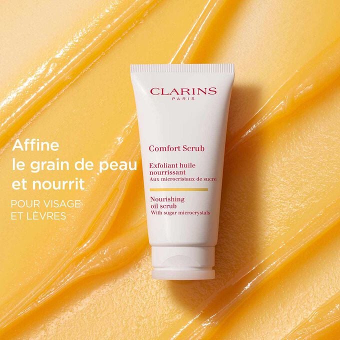 Le Comfort Scrub de Clarins pour le visage et les lèvres sur un fond texturé orange pour mettre l’accent sur son action affinante et nourrissante.