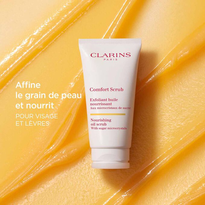 Le Comfort Scrub de Clarins pour le visage et les lèvres sur un fond texturé orange pour mettre l’accent sur son action affinante et nourrissante.