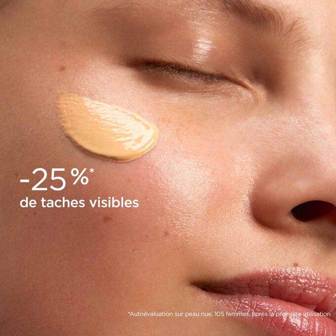 Femme yeux fermés, avec le SOS Primer Pêche de Clarins sur le visage pour illustrer qu'il réduit les taches de 25%.
