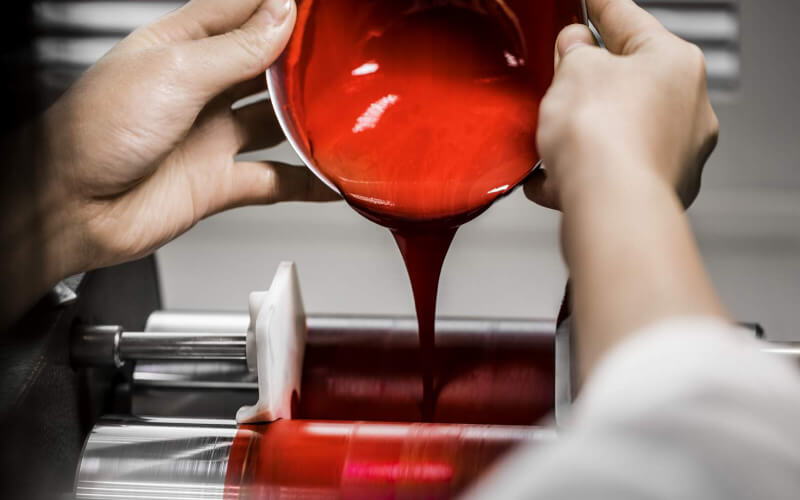 Un technicien verse une préparation crémeuse de maquillage rouge dans une machine
