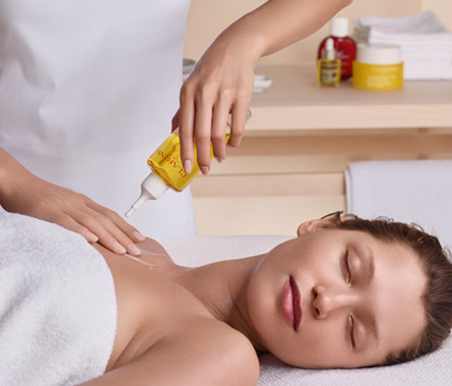 Une femme allongée qui reçoit un massage avec de l'huile Clarins 